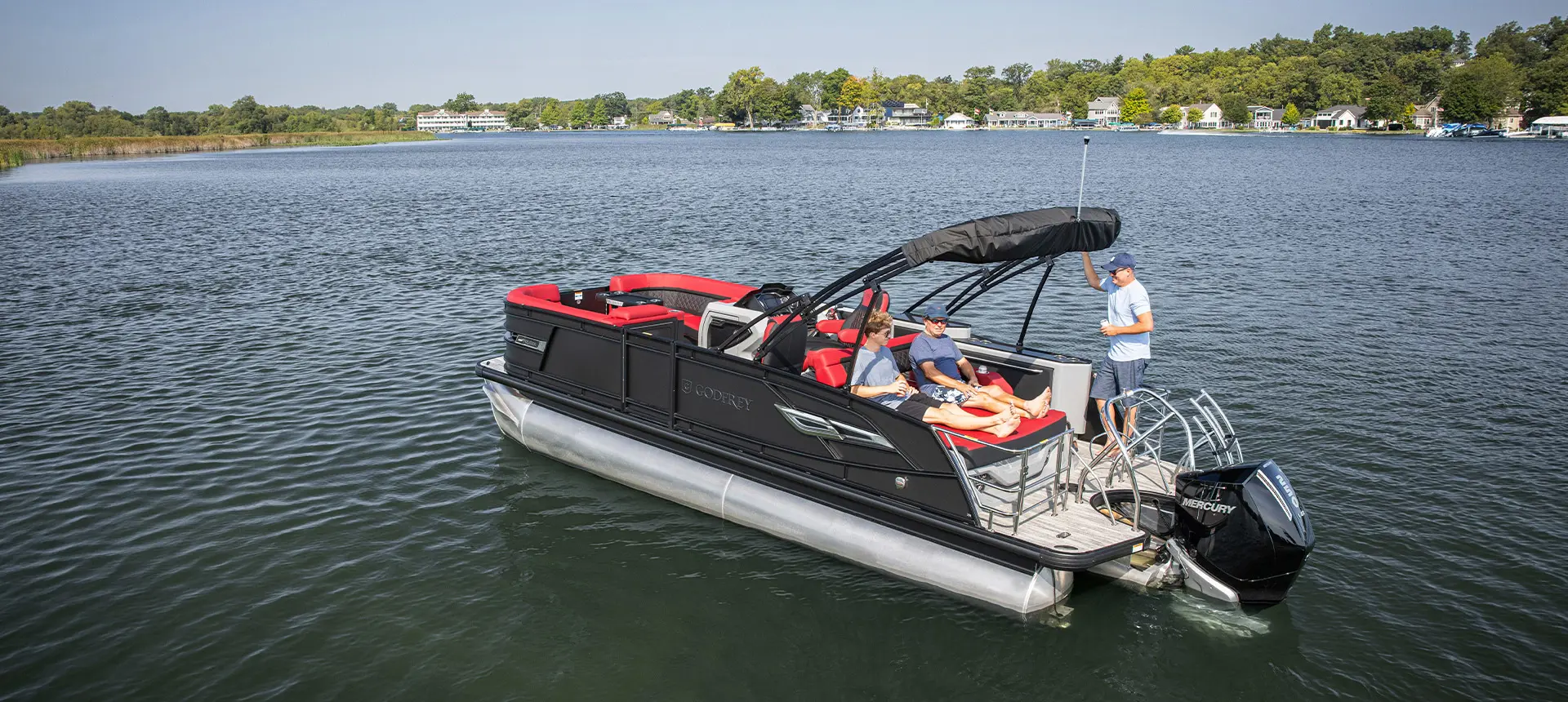 2 men sitting on the stern lounge seat while another man stands on the stern of a Godfrey AquaPatio Lounge pontoon boat.