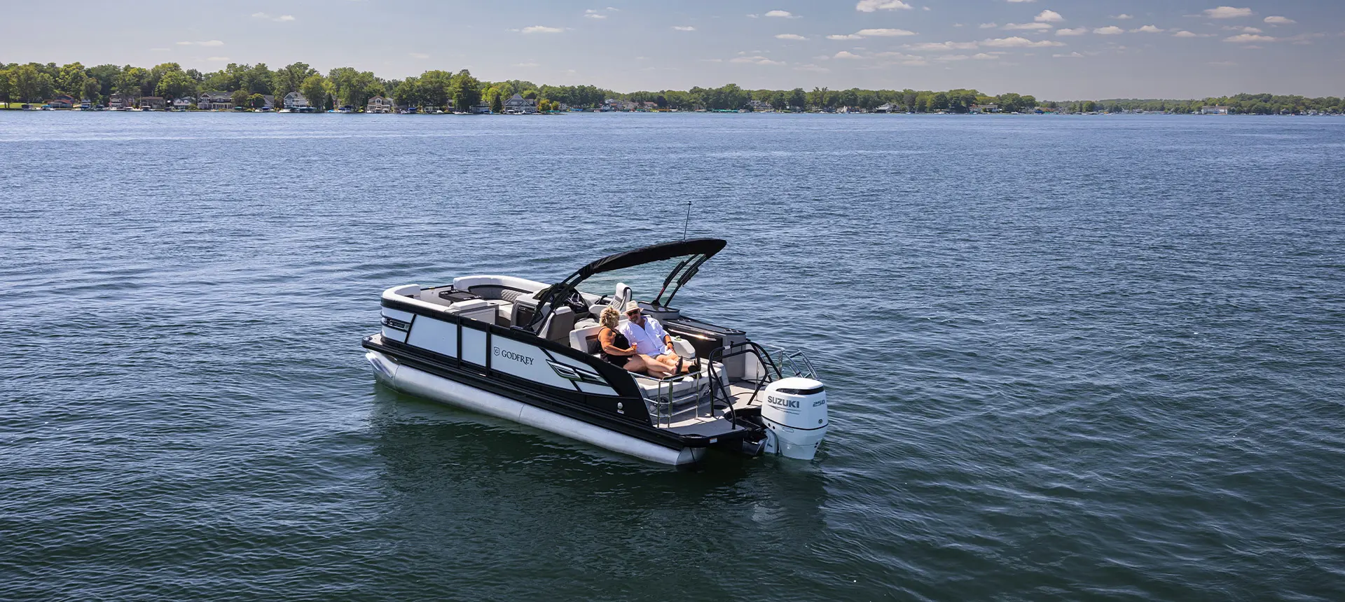 A couple relaxing together on the lake on the stern lounge seating on a Godfrey AquaPatio Lounge pontoon boat.