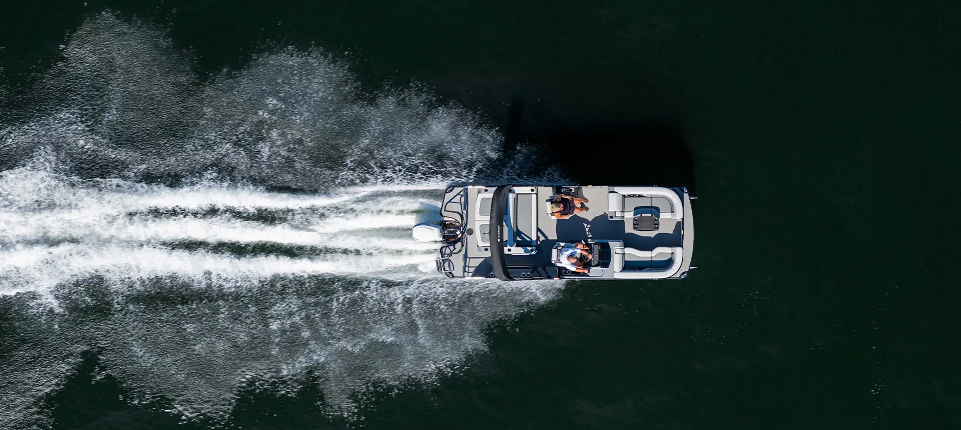 Aerial view of 2 people cruising the lake on a Godfrey AquaPatio Lounge pontoon boat.