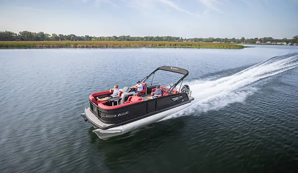 3 people on a Godfrey AquaPatio Lounge pontoon boat cruising across a lake.