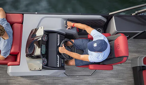 Aerial view of a man sitting at the helm of a Godfrey AquaPatio Lounge pontoon boat.
