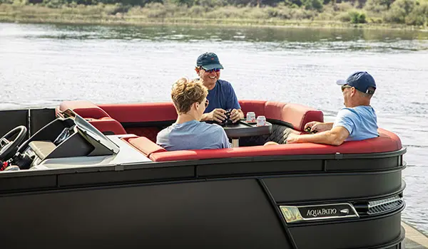 3 people playing cards at bow table on a Godfrey AquaPatio Lounge pontoon boat.