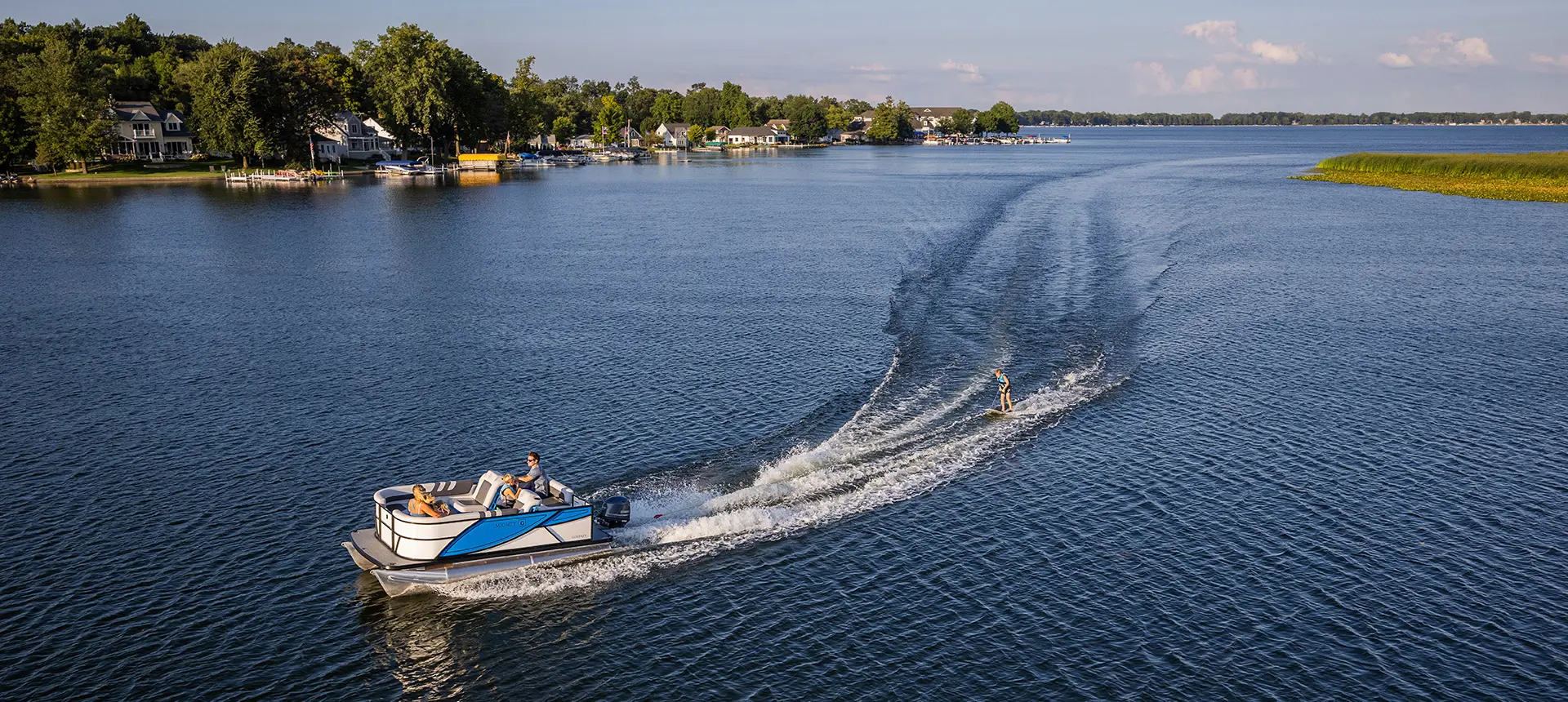 Side profile of a family on a Godfrey Mighty G Cruise pontoon boat while it pulled a wakeboarder.