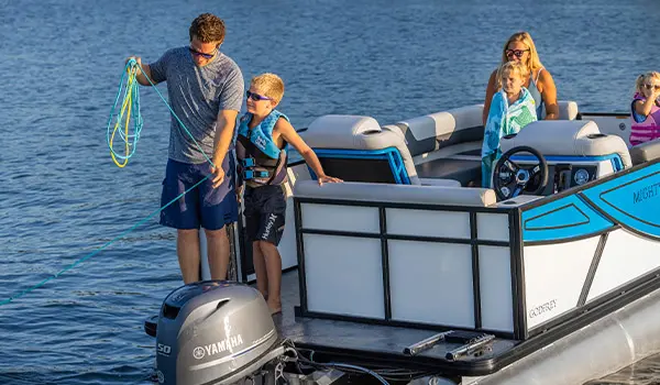 Man holding rope next to his son on the stern of a Godfrey Mighty G Cruise pontoon boat.