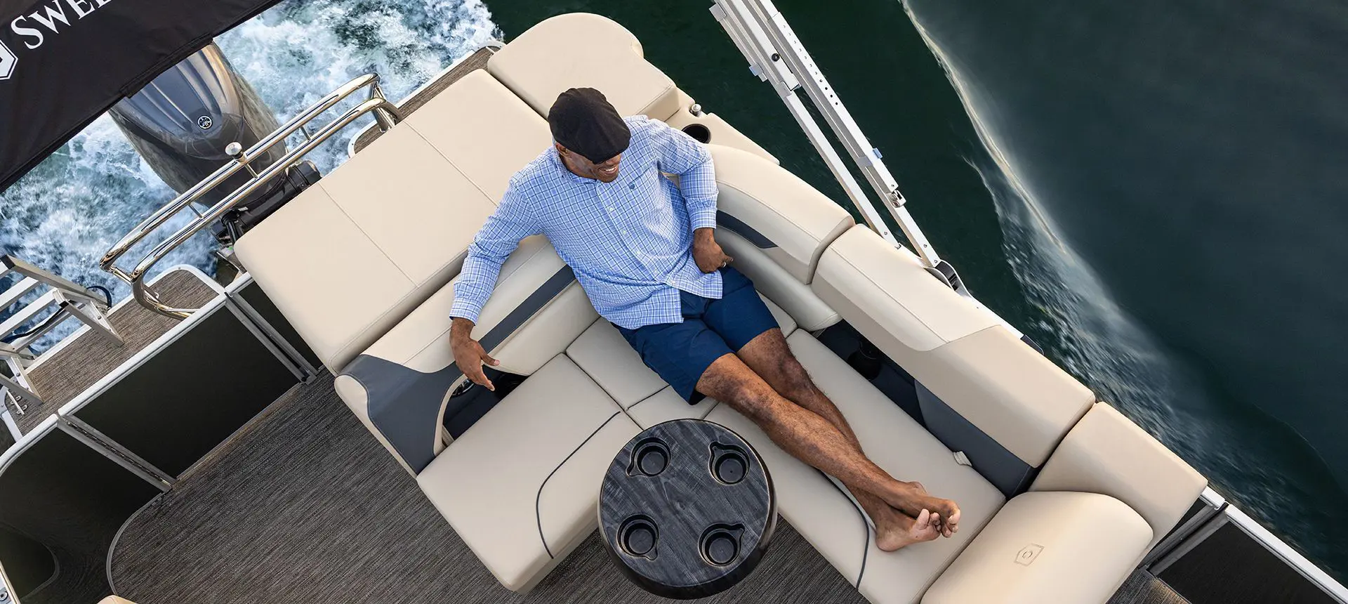 Aerial view of a man sitting on the stern seat on a Godfrey Sweetwater Cruise pontoon boat.