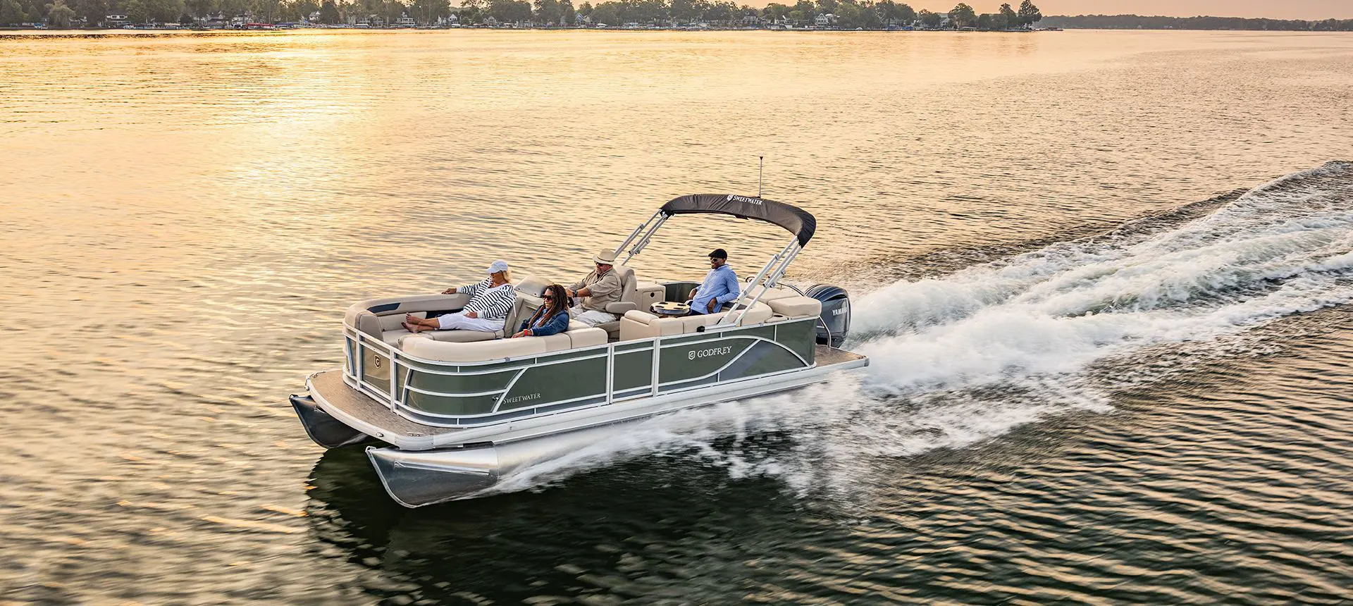 Side profile of a Godfrey Sweetwater Cruise pontoon boat cruising across a lake.