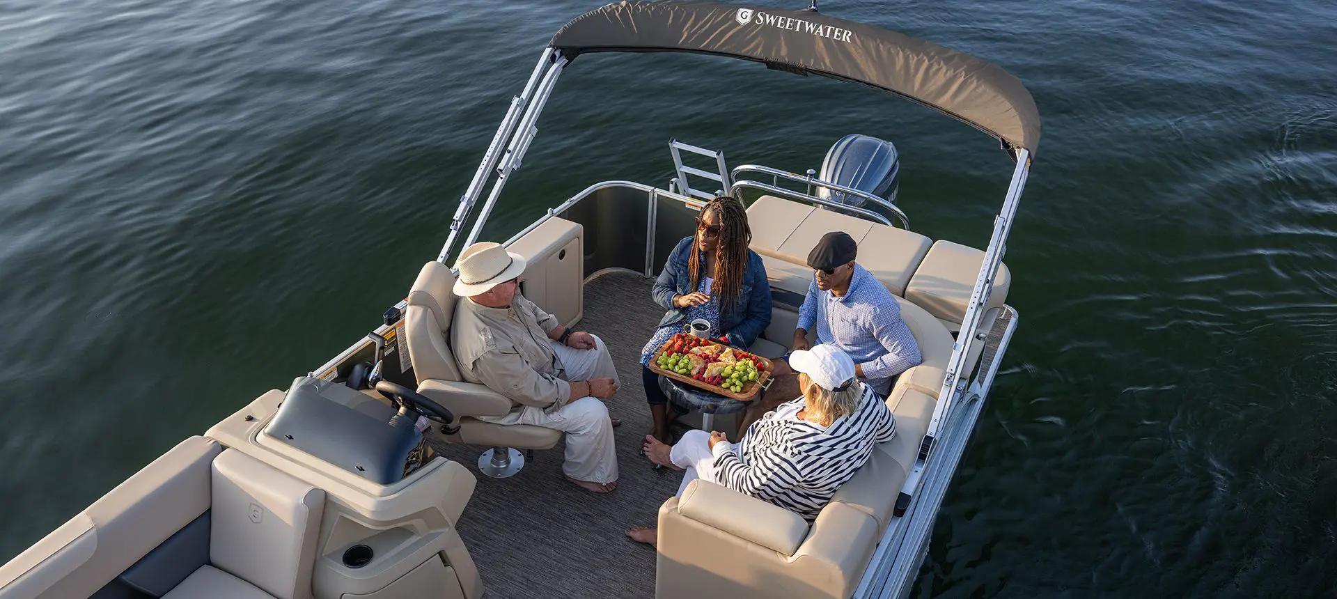 4 people having some fruit at the stern table on a Godfrey Sweetwater Cruise pontoon boat.