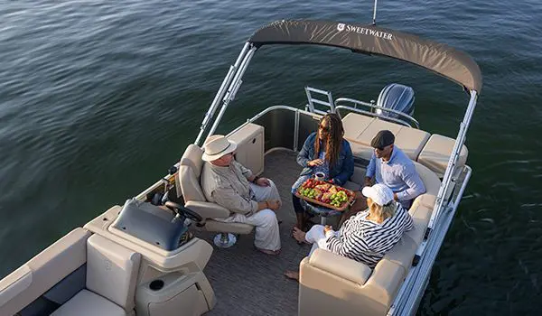 4 people having some fruit at the stern table on a Godfrey Sweetwater Cruise pontoon boat.