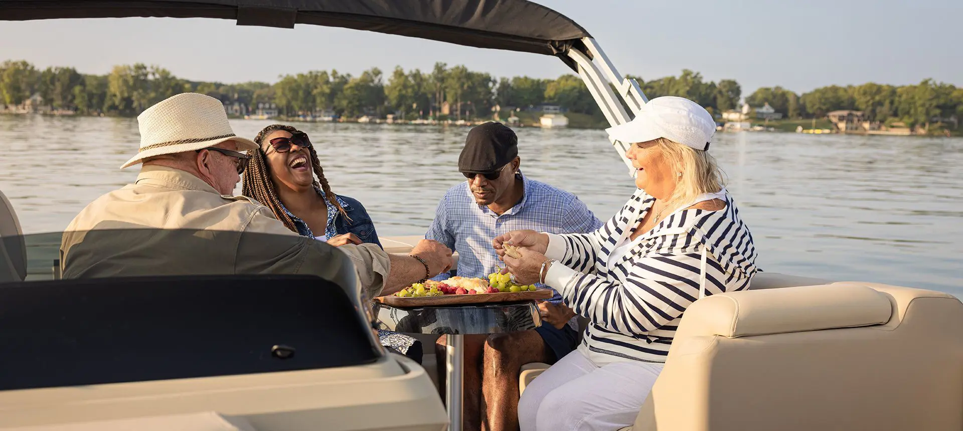 4 people having a laugh and enjoying some fruit at the stern table on a Godfrey Sweetwater Cruise pontoon boat.