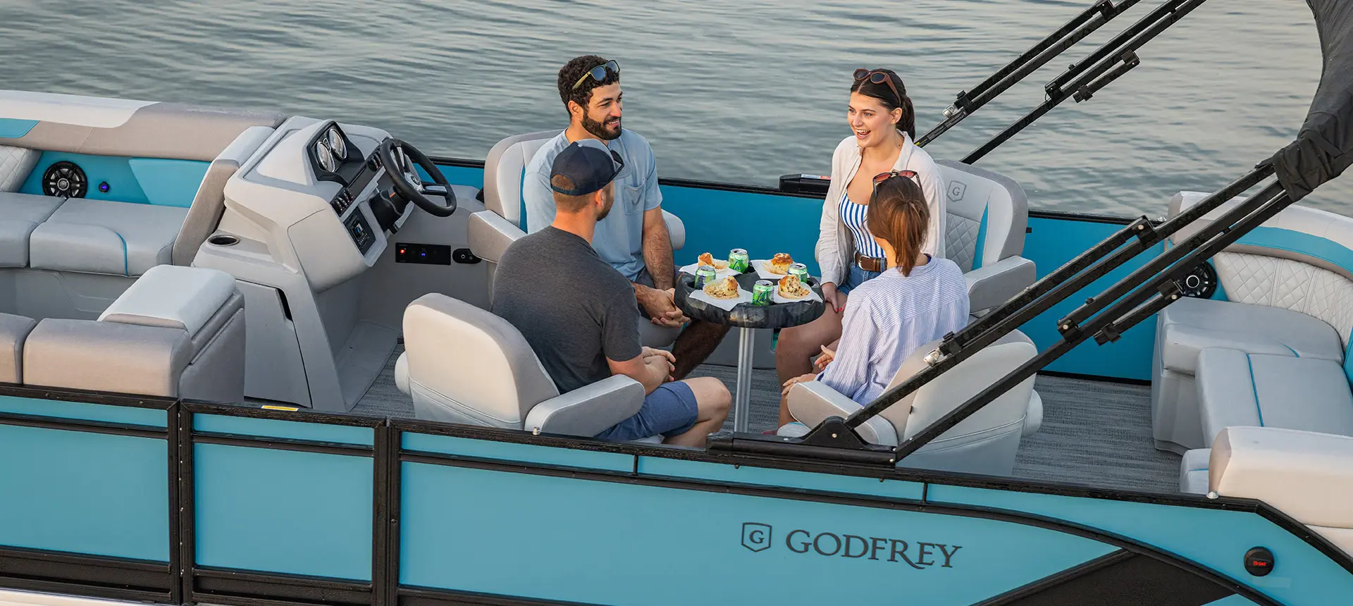 Side profile of a Godfrey Sweetwater Entertainment pontoon boat floating on a lake at sunset.