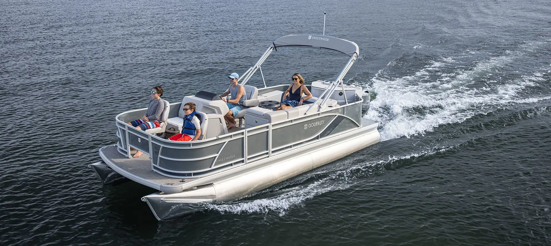 Side profile of a Godfrey Sweetwater Fishing pontoon boat cruising on a lake.