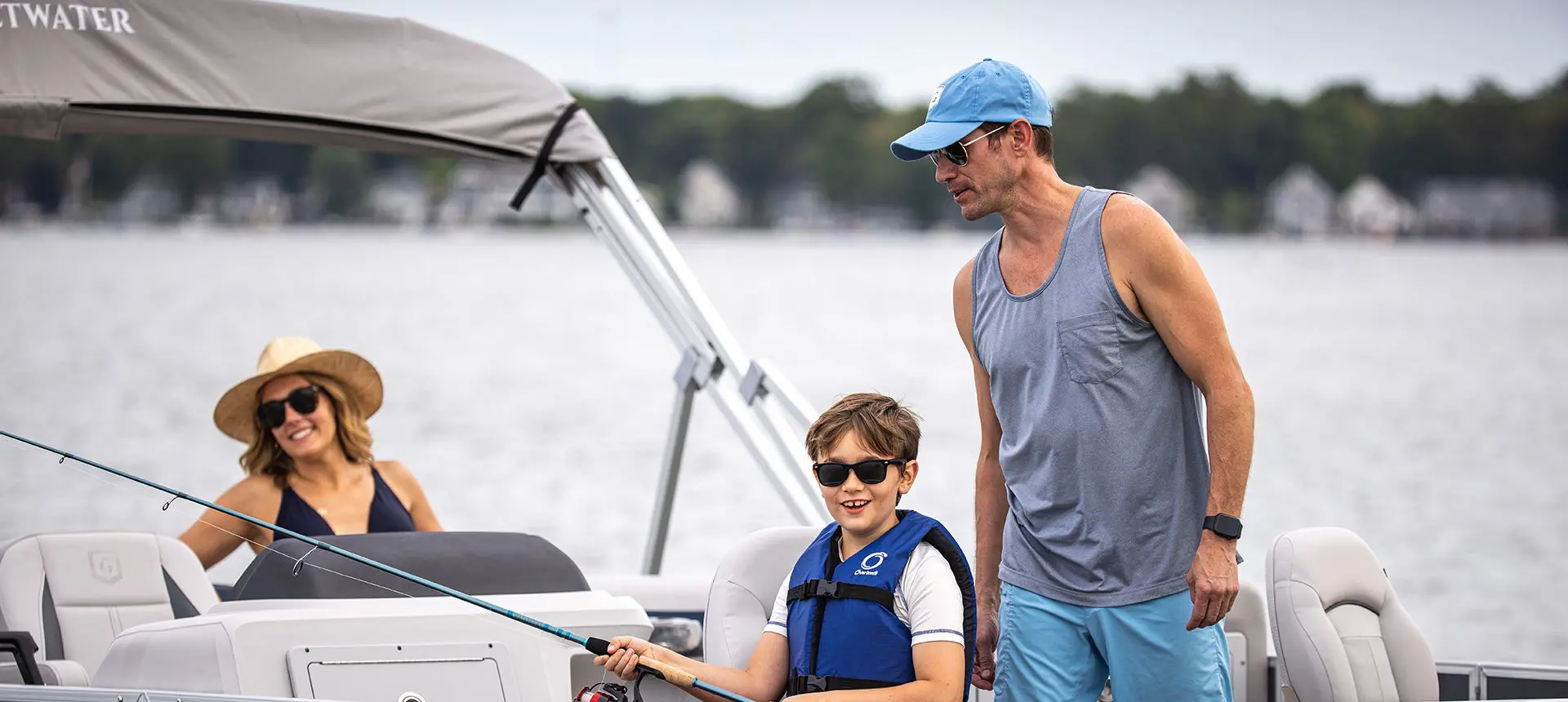 Dad helping his son fish off a Godfrey Sweetwater Fishing pontoon boat while mom watches in the background.
