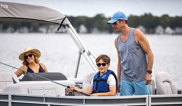 Dad helping his son fish off a Godfrey Sweetwater Fishing pontoon boat while mom watches in the background.