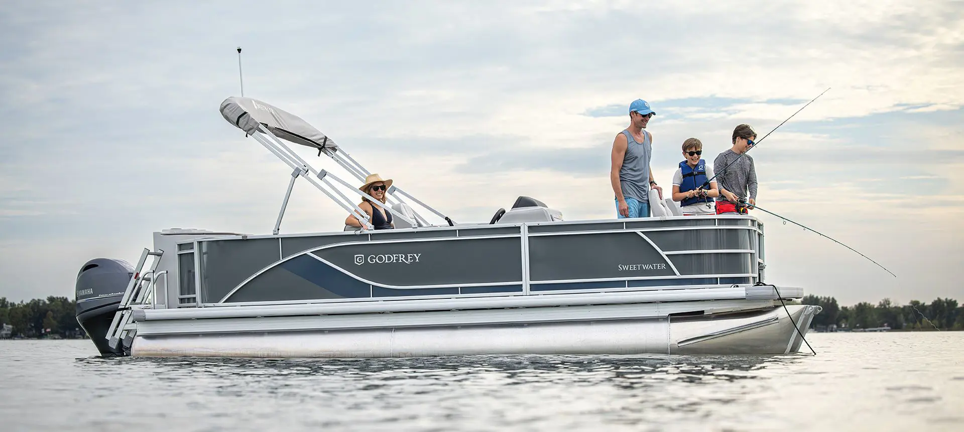 2 boys fishing off the bow of a Godfrey Sweetwater Fishing pontoon boat while their parents watch.