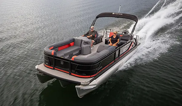 Bow focused aerial view of a couple cruising the lake on a Godfrey Sweetwater Lounge pontoon boat.