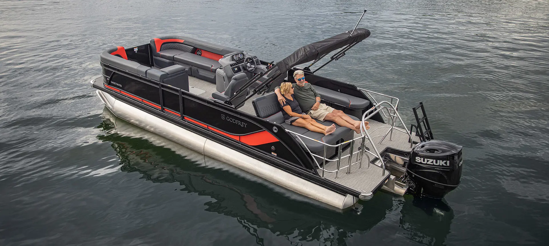 A couple relaxing on the stern lounge seating on a Godfrey Sweetwater Lounge pontoon boat.