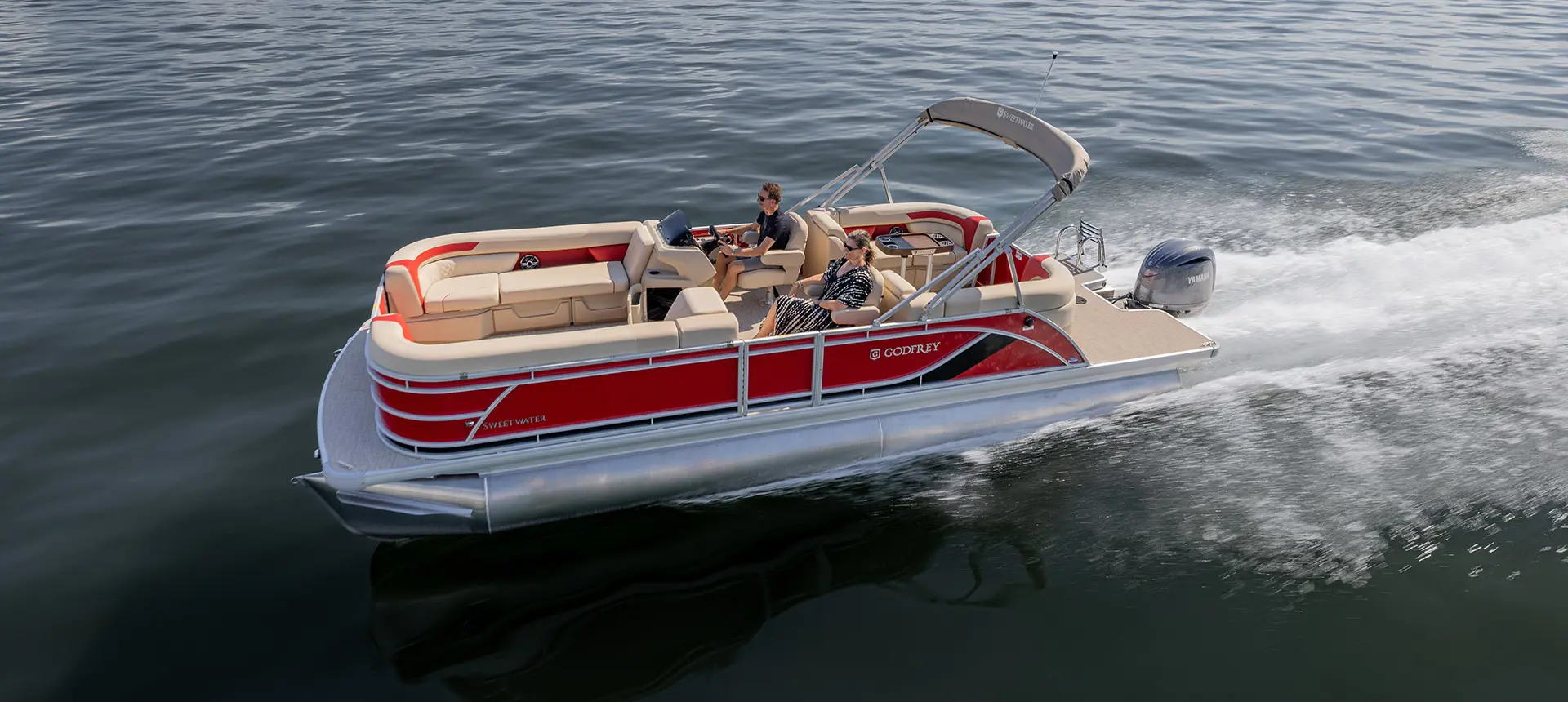 Side profile of a Godfrey Sweetwater Split Bench pontoon boat cruising across a lake.