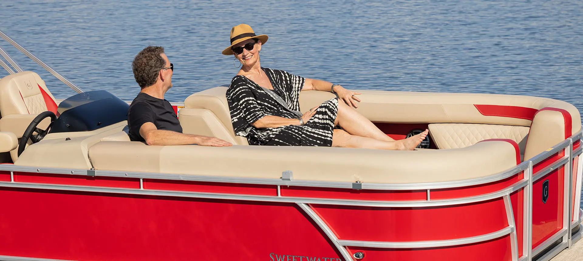 A couple relaxing on the bow seating of a Godfrey Sweetwater Split Bench pontoon boat.