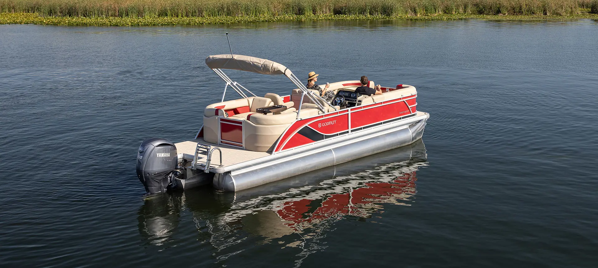 Side/stern focused view of a Godfrey Sweetwater Split Bench pontoon boat floating on a lake.