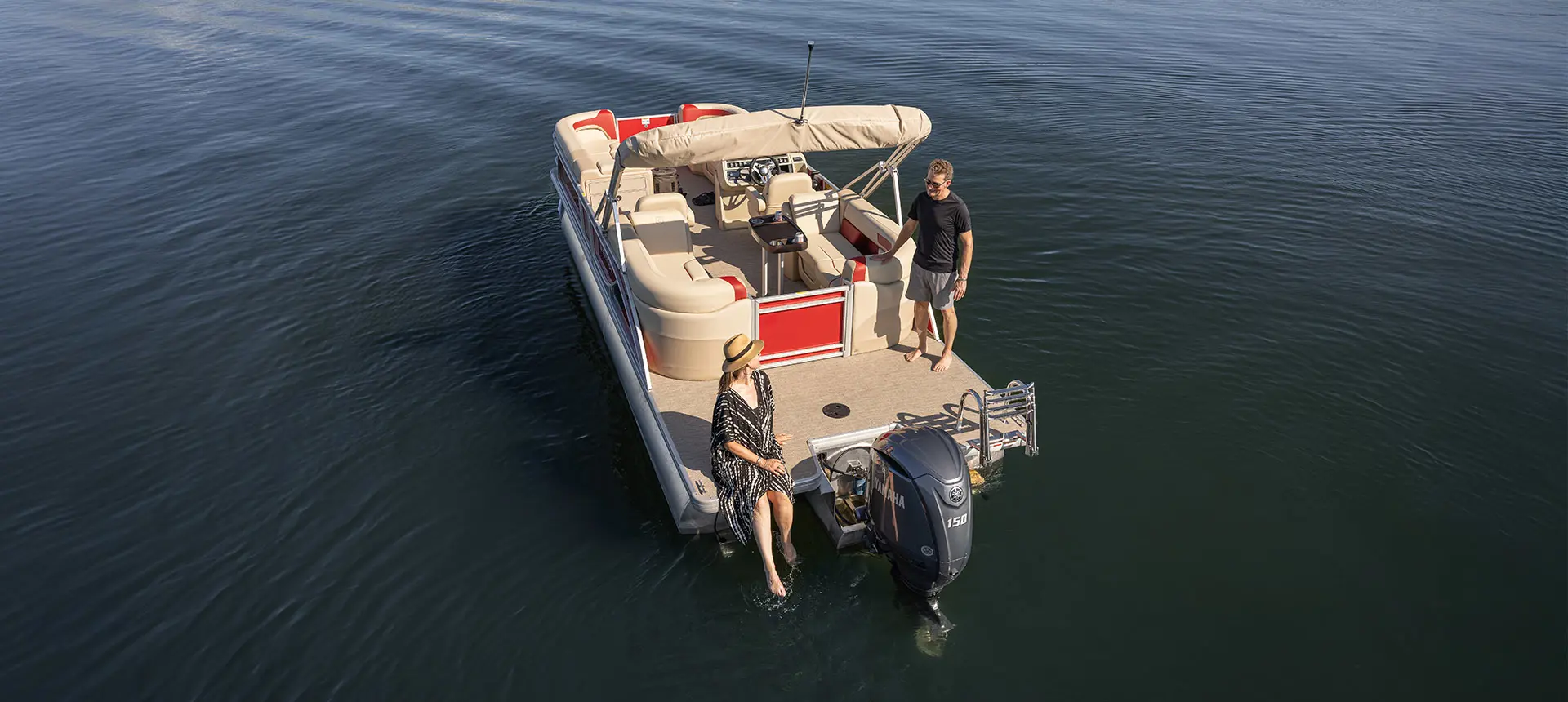 Aerial view of a couple relaxing on the stern of a floating Godfrey Sweetwater Split Bench pontoon boat.