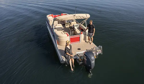 Aerial view of a couple relaxing on the stern of a floating Godfrey Sweetwater Split Bench pontoon boat.