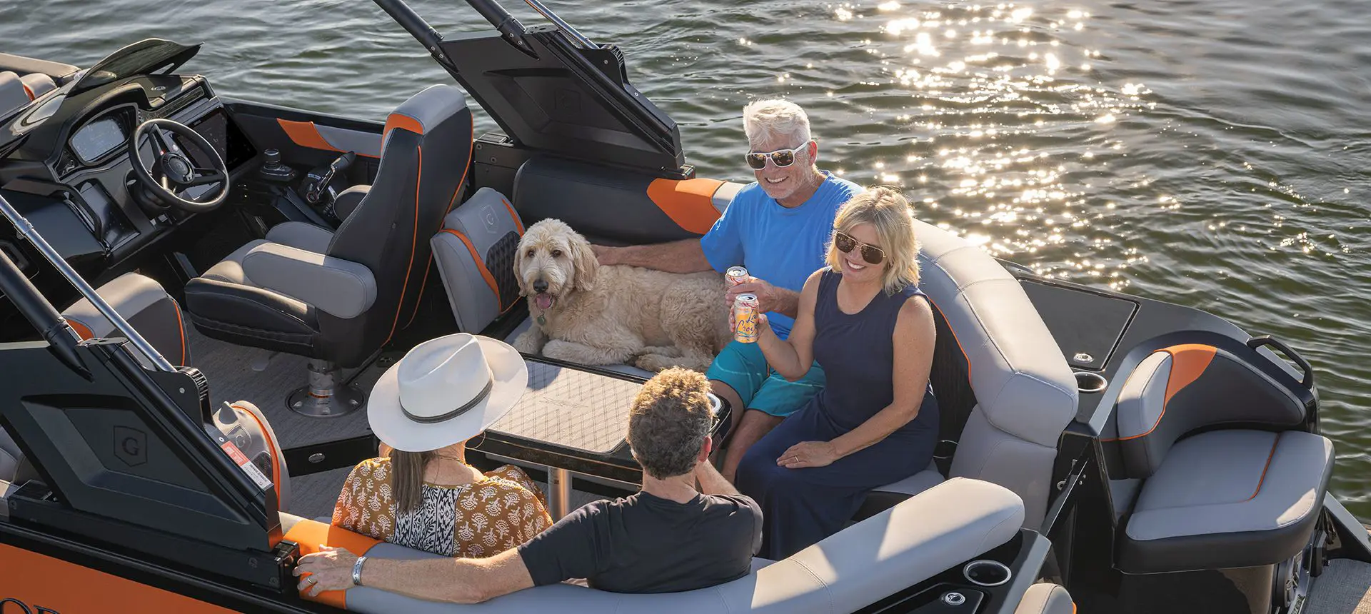 2 couples and a dog relaxing and enjoying a beverage on the stern table of a Godfrey XP Tritoon boat.