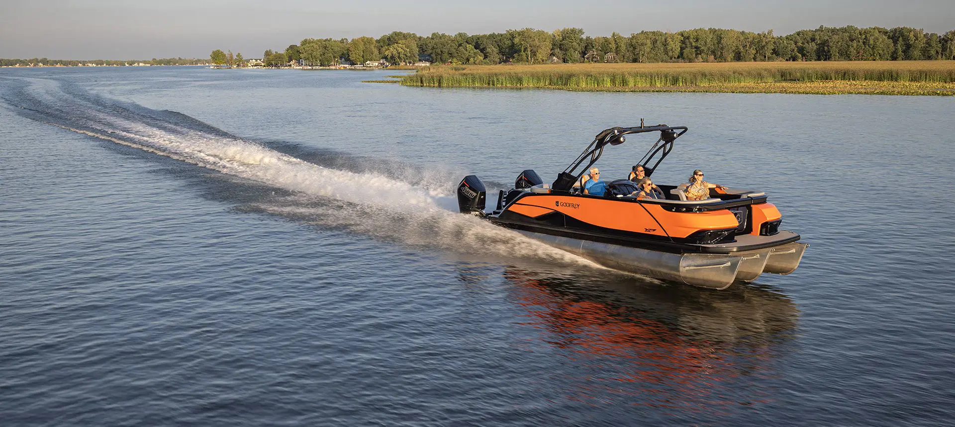 An orange Godfrey XP Tritoon boat cruising on a lake with 4 passengers on board.