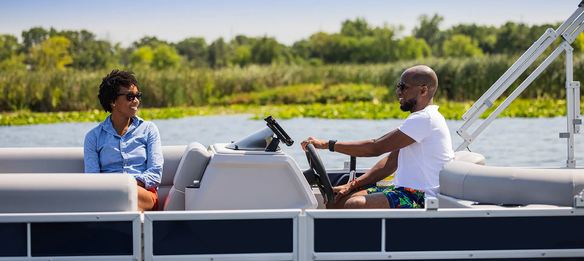 Woman smiling at her partner while he's at the helm of a Godfrey Xperience Cruise pontoon boat.