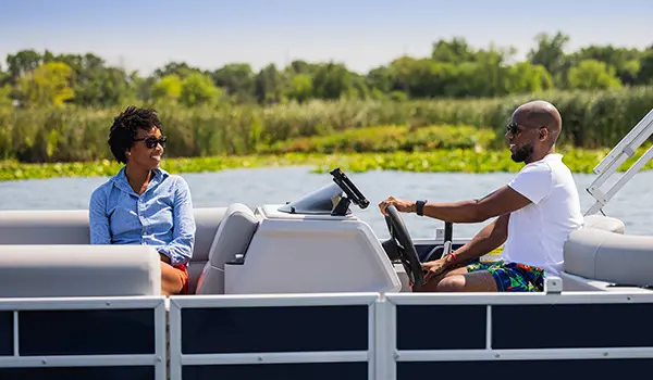 Woman smiling at her partner while he's at the helm of a Godfrey Xperience Cruise pontoon boat.