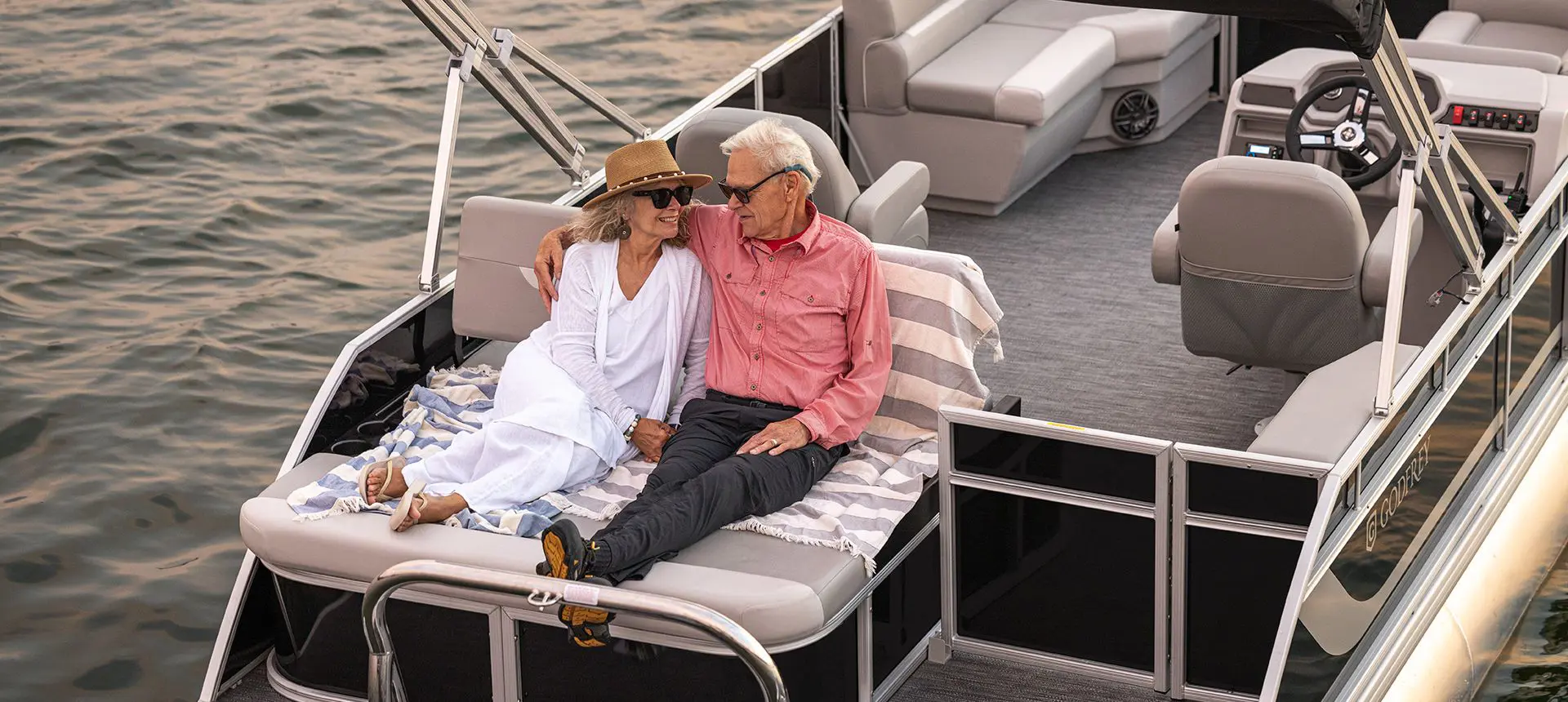 A couple cuddling on the stern lounge seat on a Godfrey Xperience Lounge pontoon boat.