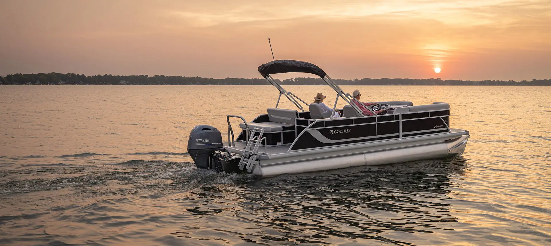 Side profile of a Godfrey Xperience Lounge pontoon boat floating on the lake at sunset.