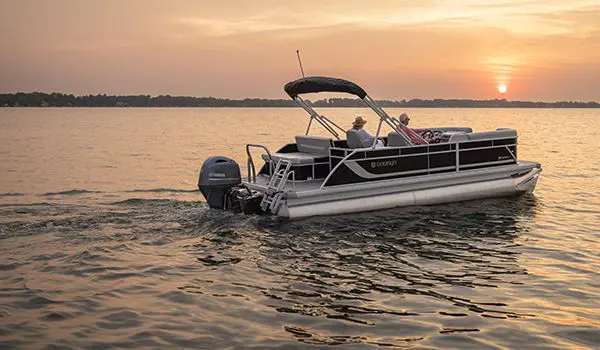 Side profile of a Godfrey Xperience Lounge pontoon boat floating on the lake at sunset.