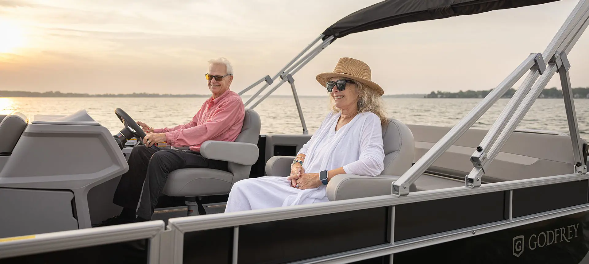 A couple smiling while cruising the lake on their Godfrey Xperience Lounge pontoon boat.