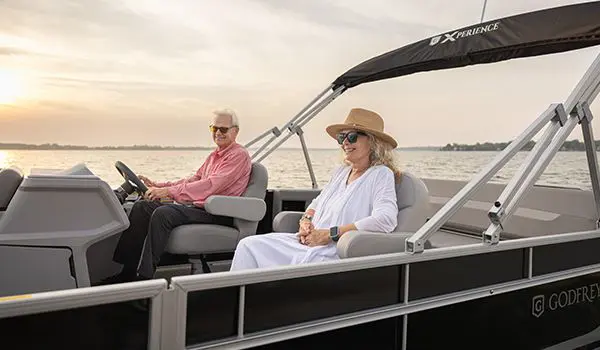 A couple smiling while cruising the lake on their Godfrey Xperience Lounge pontoon boat.