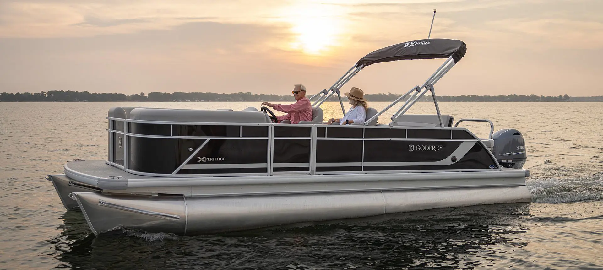 Side profile of a Godfrey Xperience Lounge pontoon boat on the lake at sunset.