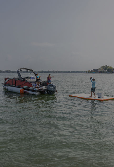 Godfrey pontoon boat on a lake with an inflatable swim platform and people enjoying recreational activities.