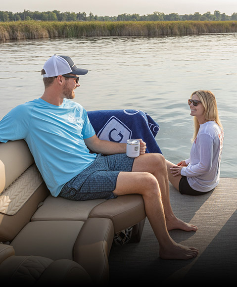 Woman sitting on pontoon next to Bennington bag and towels. 