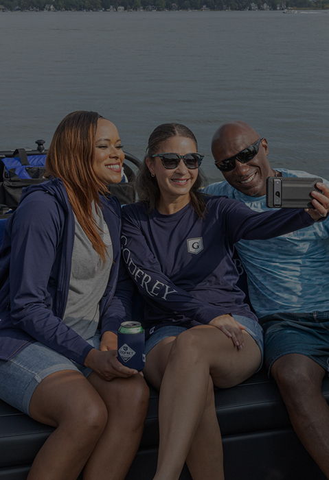Three people taking a selfie on a Godfrey pontoon boat, with one person wearing a Godfrey branded long-sleeve shirt.