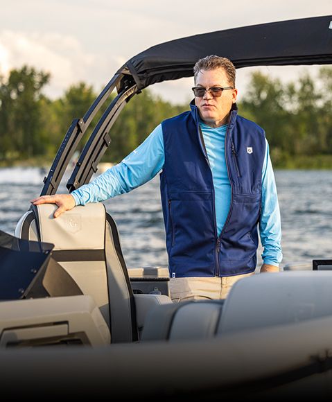 Man standing on pontoon boat wearing a blue Godfrey vest. 
