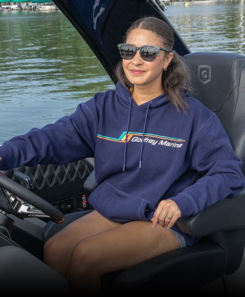 Woman smiles in captains chair of a pontoon boat while wearing a dark blue Bennington sweatshirt. 