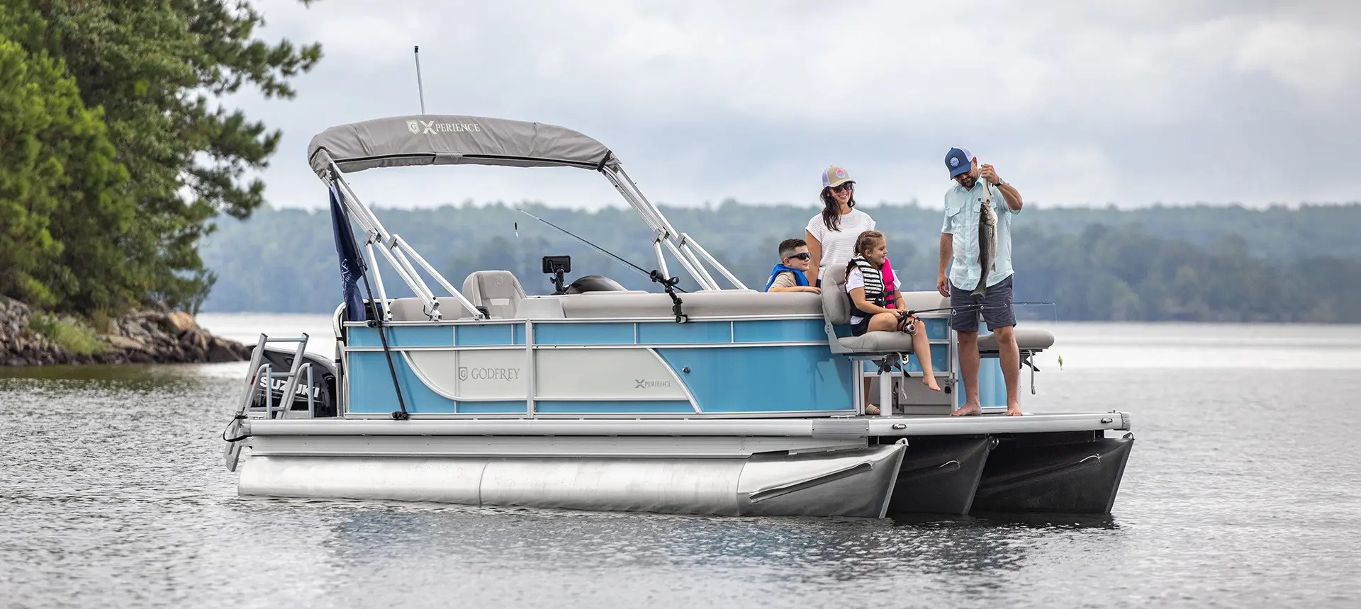 Man shows fish he caught to family on the front of a Godfrey Pontoon boat.