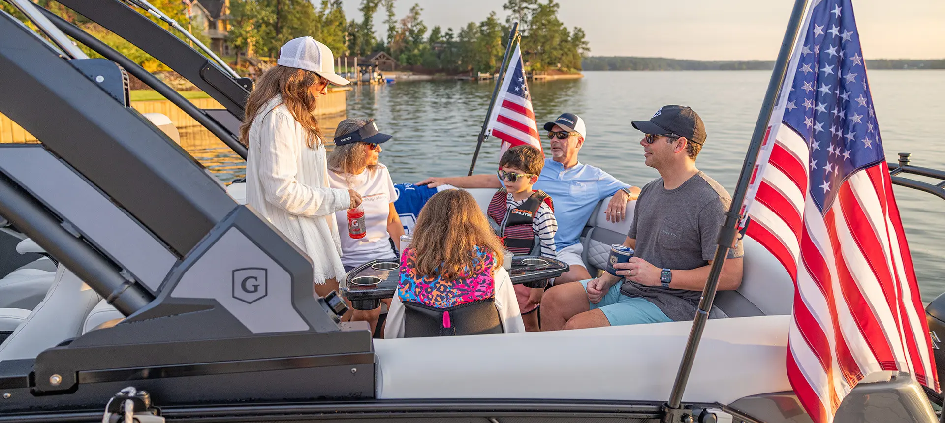 Family lounges on the front of a pontoon boat with American flags attached by a toolless boat accessory attachment system.