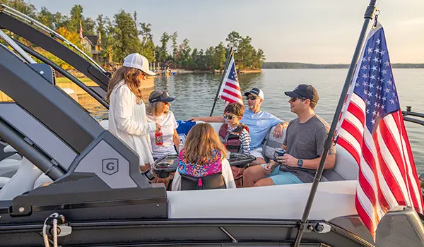 Family lounges on the front of a pontoon boat with American flags attached by a toolless boat accessory attachment system.