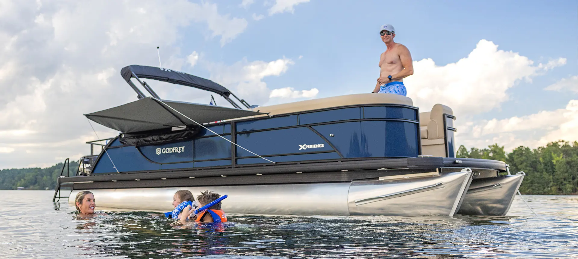 Family lounges on the front of a pontoon boat with American flags attached by a toolless boat accessory attachment system.