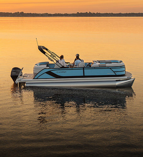 Side-view of a Godfrey Pontoon boat parked on lake during sunset. 