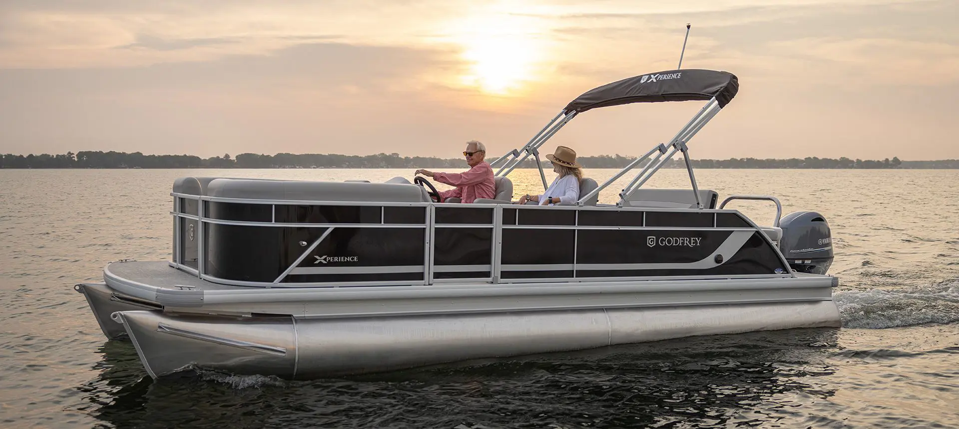 Side profile of a Godfrey Xperience pontoon boat cruising on a lake.