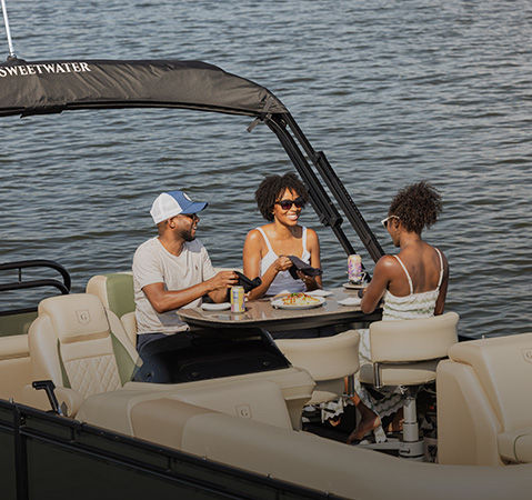 3 people enjoying a snack at the Mid-Table on a Godfrey pontoon boat with a Mid-Table (MT) layout.