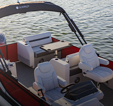 A Godfrey pontoon boat with a Dinette Table (DT) layout floating on a lake.