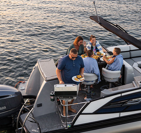 A man serving food to his family from the optional built-in grill on a Godfrey pontoon boat with an entertainment layout.