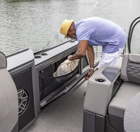 A man grabbing gear from the ample storage on a Godfrey pontoon boat with an entertainment layout.